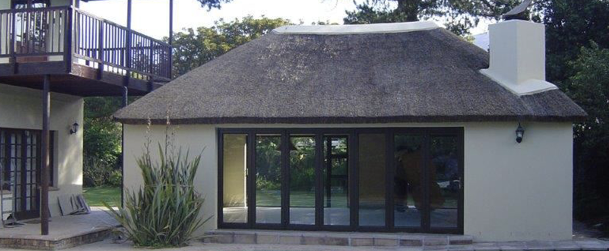 Thatched braai room with full-height sliding doors and white rendered walls, Cape Town